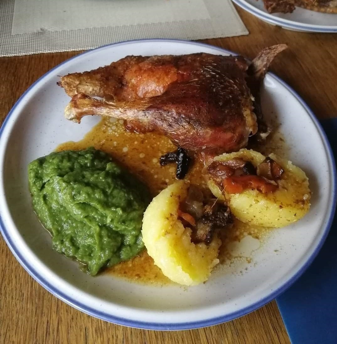 A plate featuring a succulent piece of roasted duck, a sliced potato dumpling bathed in rich gravy, and a serving of creamy savoy cabbage puree, also known as 'Wirsing.