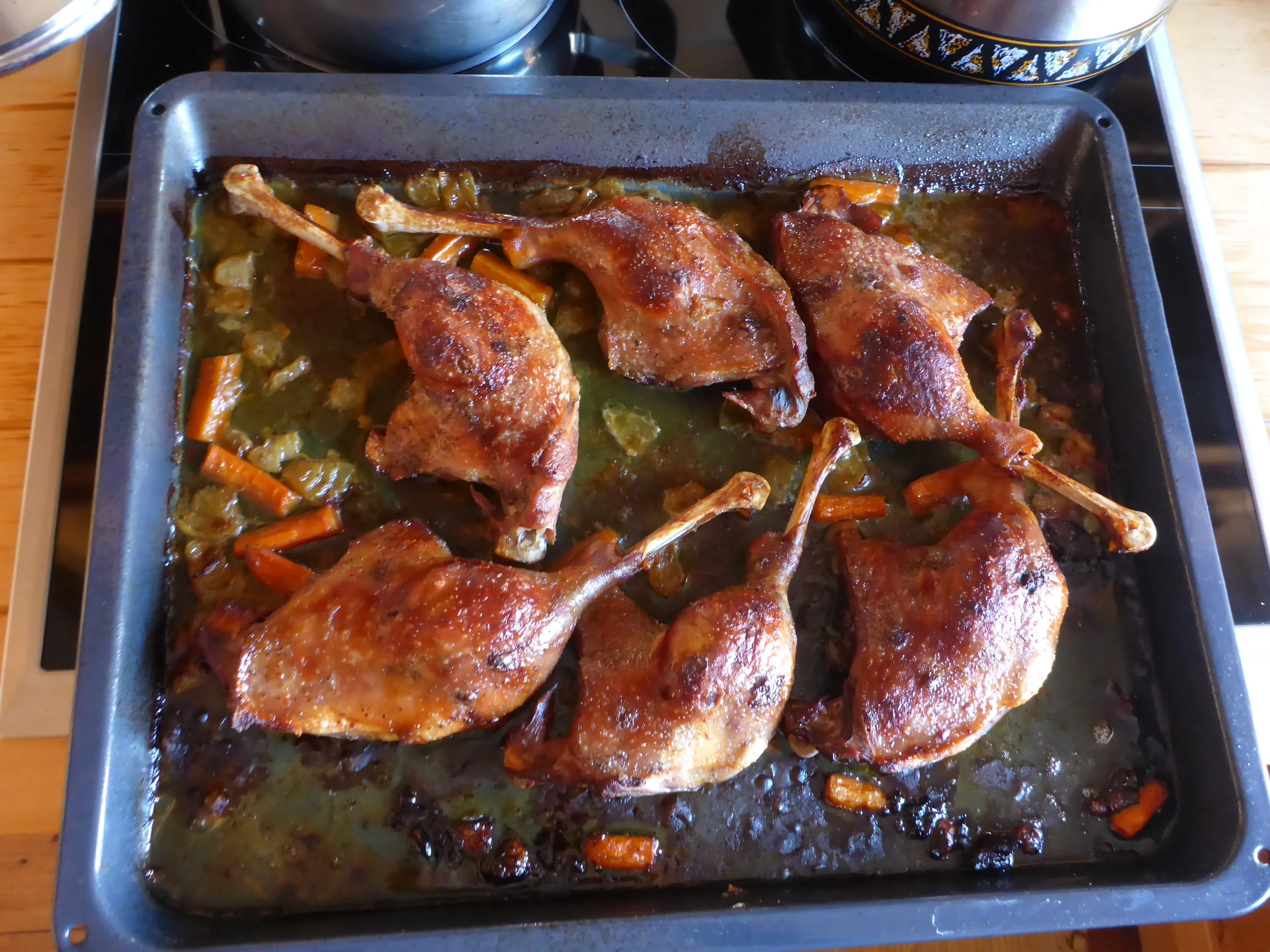 German roasted Goose legs, carrots and onions on a baking sheet with beautifully crispy skin after roasting.