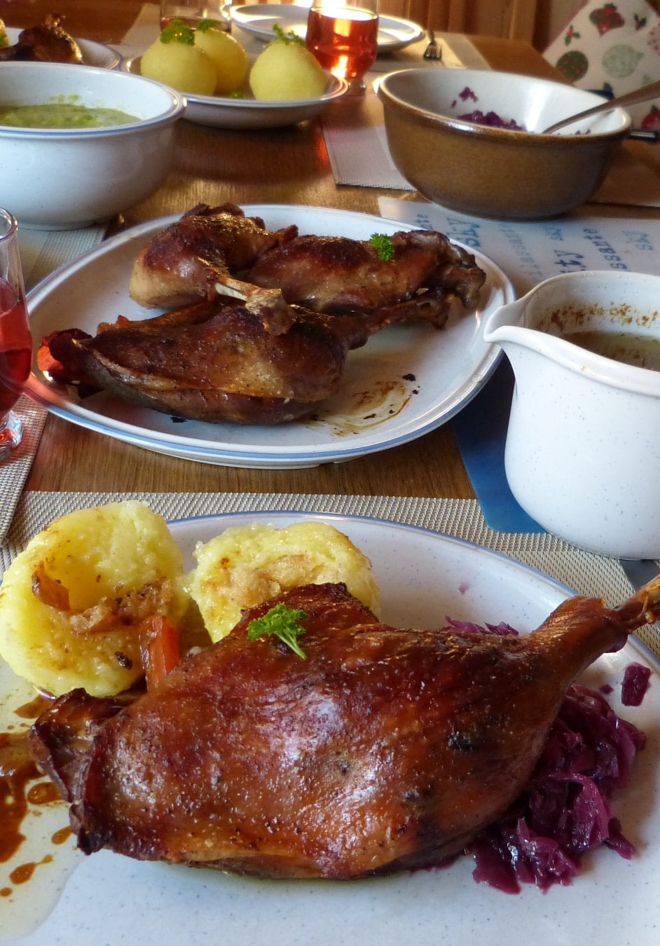 Nicely golden brown German roasted  goose leg served on a plate with potato dumplings, rich gravy from the drippings, and blaukraut (red cabbage).