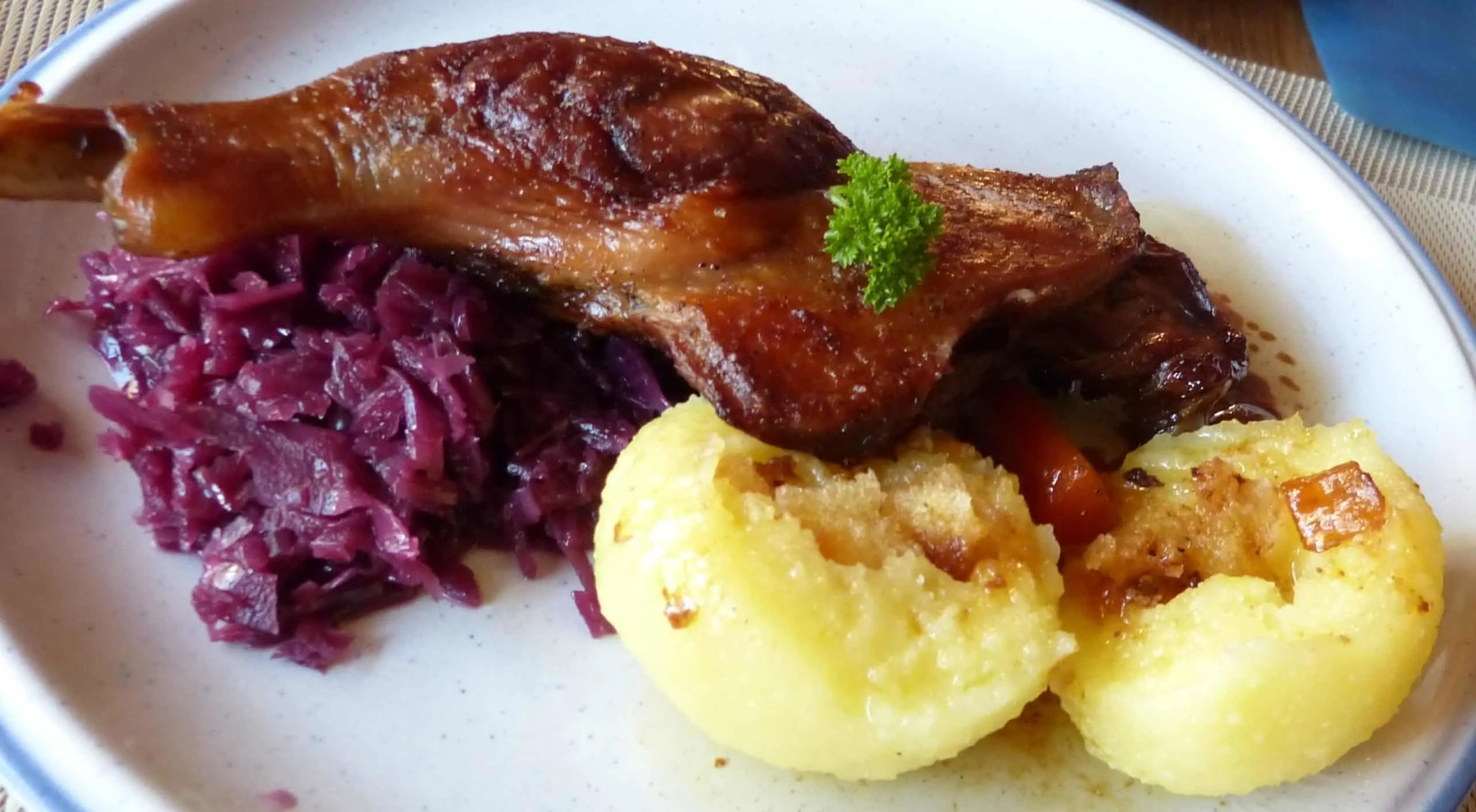 Nicely golden brown German roasted goose leg served on a plate with potato dumplings, rich gravy from the drippings, and blaukraut (red cabbage).