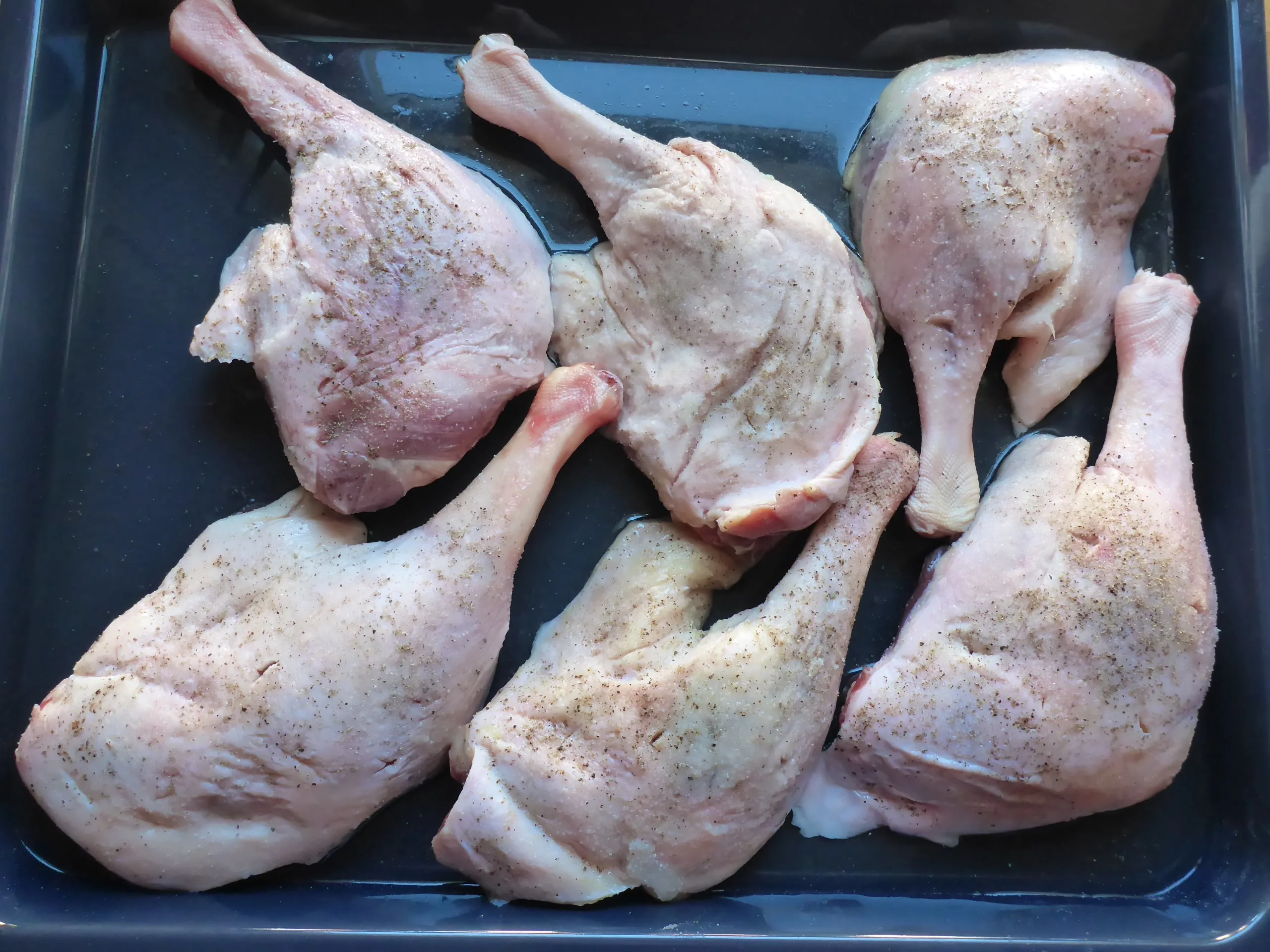 Goose legs arranged on a baking sheet before being placed in the oven to cook.