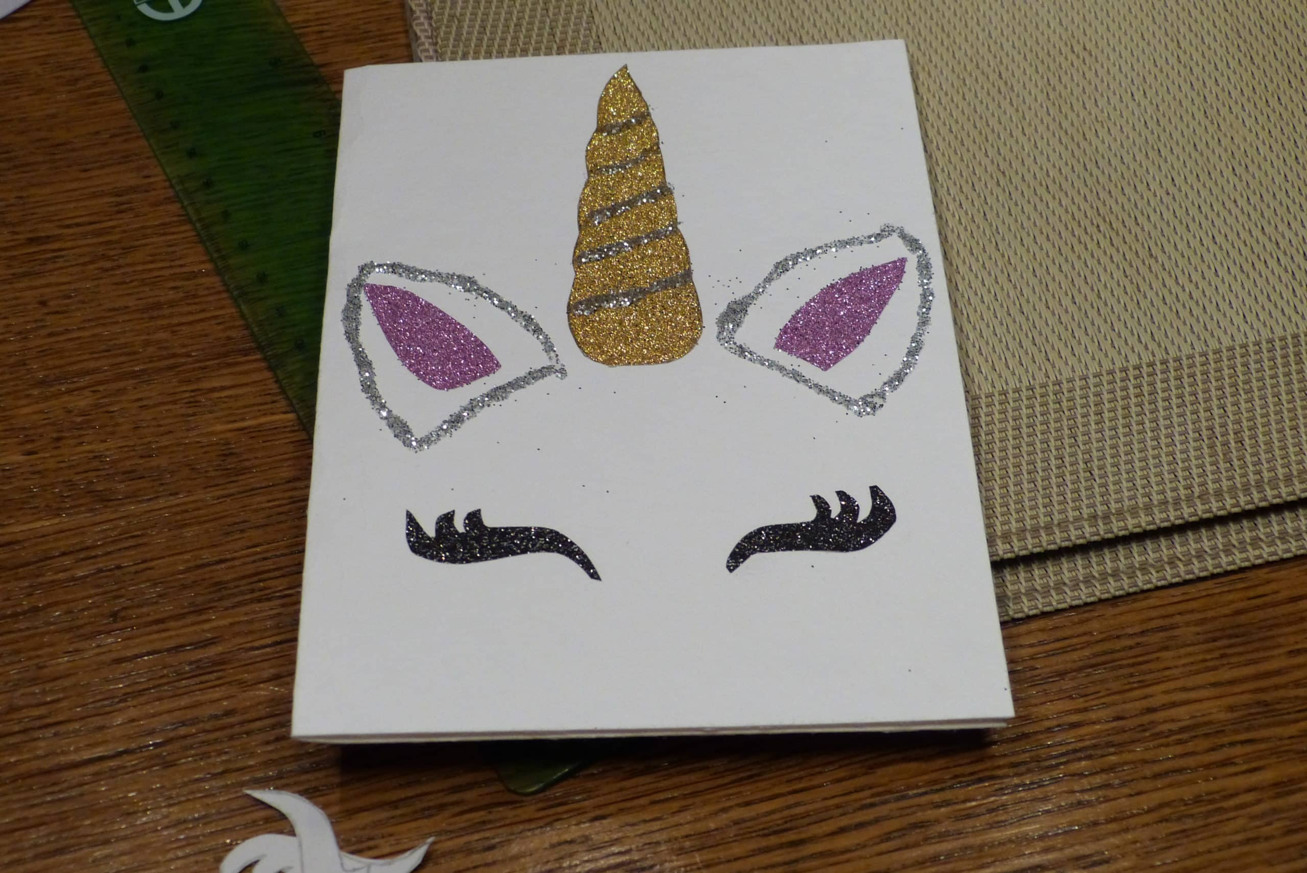 Eine kreative Einhorn-Einladung mit einem zauberhaften Einhorn-Kopf aus Glitzerpapier, verziert mit Glitzer-Ohrmuscheln und funkelnden Wimpern.