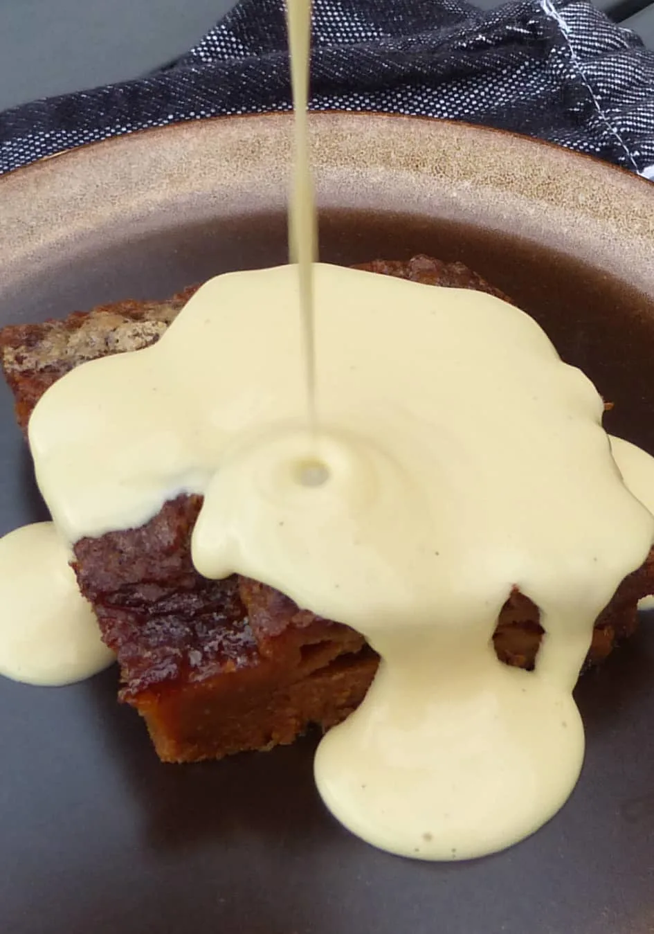 Ein Bild von einem süßen Dessert: Malva Pudding, über den gerade köstliche Vanillesoße gegossen wird.