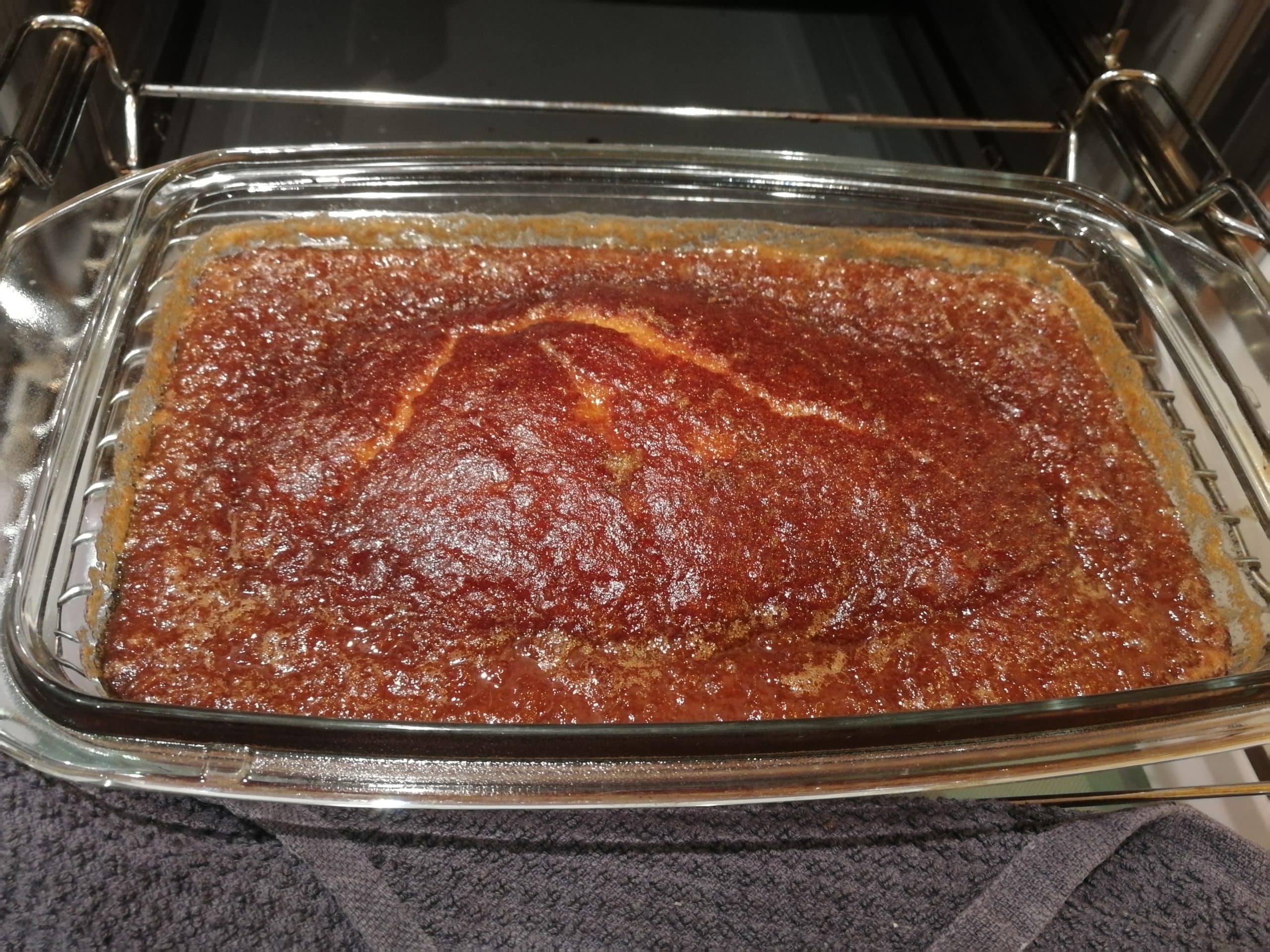 Ein Bild von einem perfekt gebackenen Malva Pudding in einer Auflaufform, mit einer wunderschönen, karamellisierten, dunkelbraunen Oberfläche, nachdem er den köstlichen Sirup aufgesogen hat.