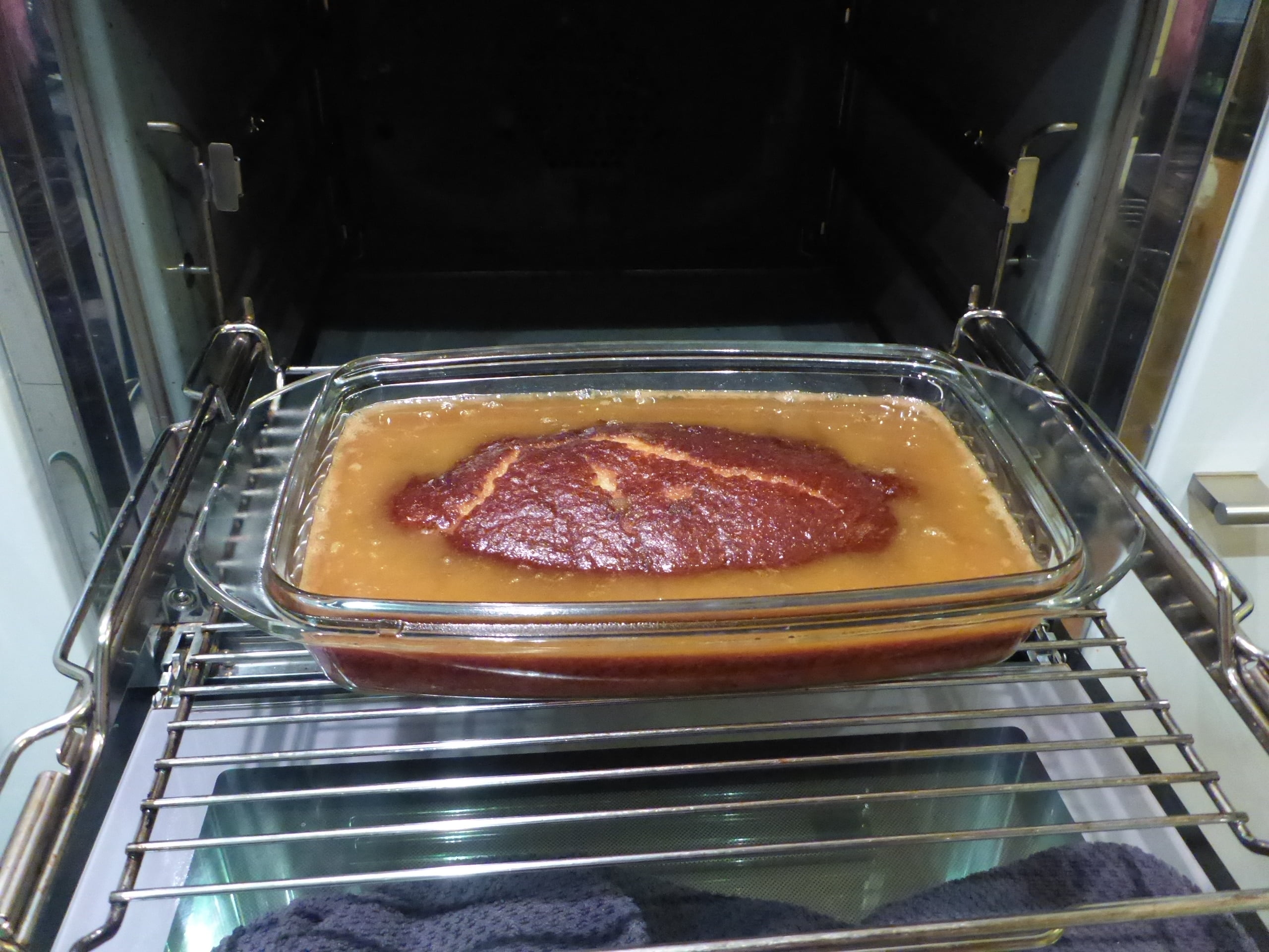 Ein Bild von einem frisch gebackenen Malva Pudding, der gerade aus dem Ofen genommen wurde. Eine Gabel hat gerade Löcher in den Pudding gestochen, und jetzt wurde köstlicher Sirup darüber gegossen.