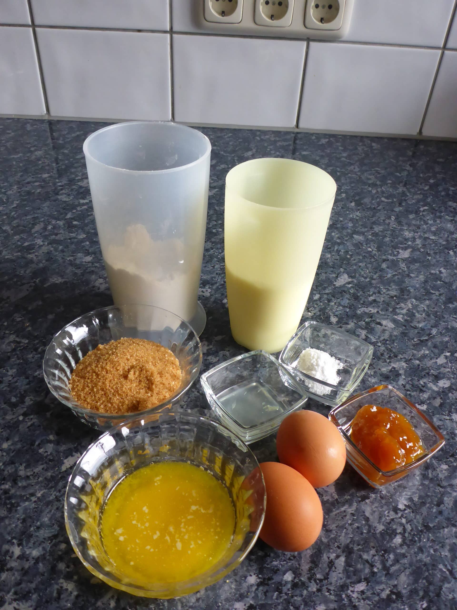 Ein Bild von den Zutaten für den Malva Pudding-Teig, darunter Mehl, Zucker, Eier, Milch, Butter, Aprikosenmarmelade  und Natron.