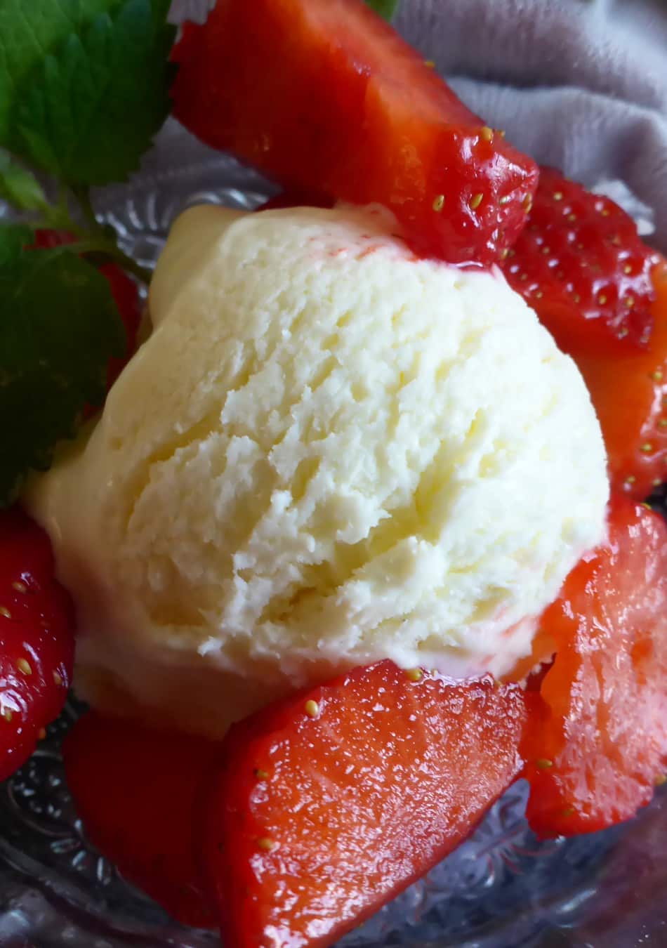 A bowl of homemade vanilla ice cream topped with fresh strawberry slices and beautifully garnished with lemon balm.