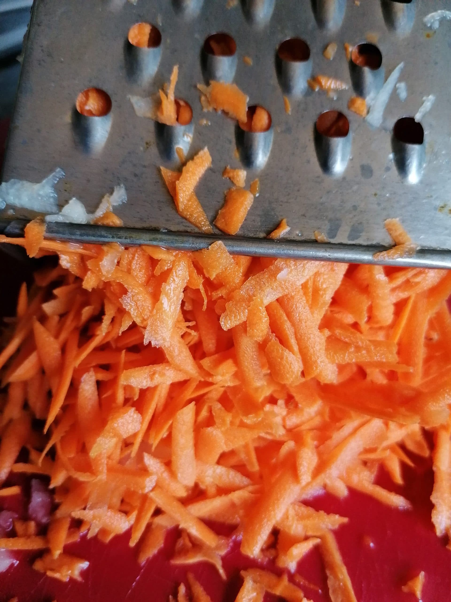 A close-up photo capturing the culinary process of grating peeled carrots on a box grater. The vibrant orange carrots are being transformed into fine, grated strands, perfect for adding delightful sweetness and color to a delicious dish.