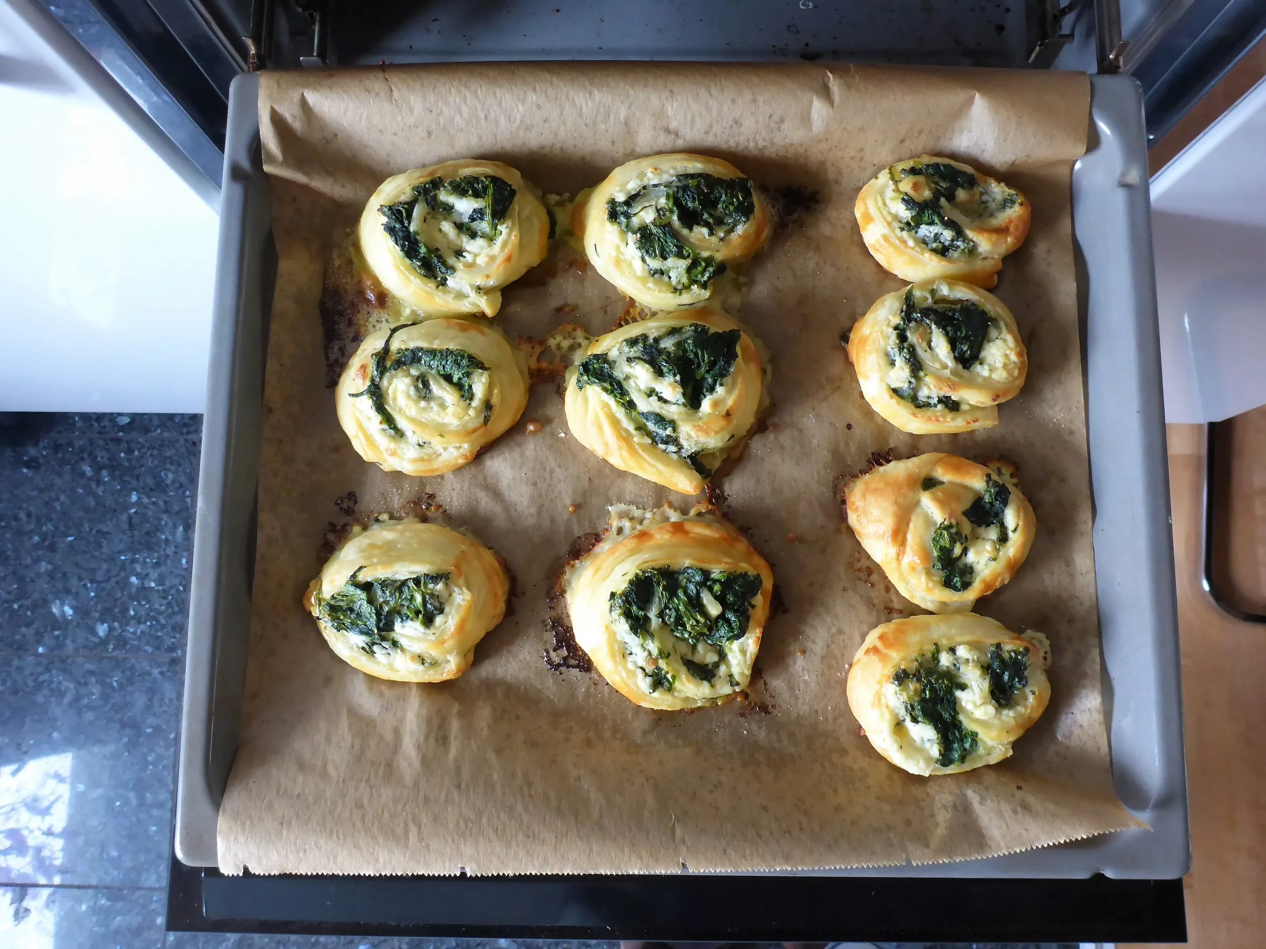 Auf dem Bild sind frisch gebackene Spinat und Feta Blätterteigschnecken  vegetarisch  zu sehen, die auf einer Tellerplatte sind.