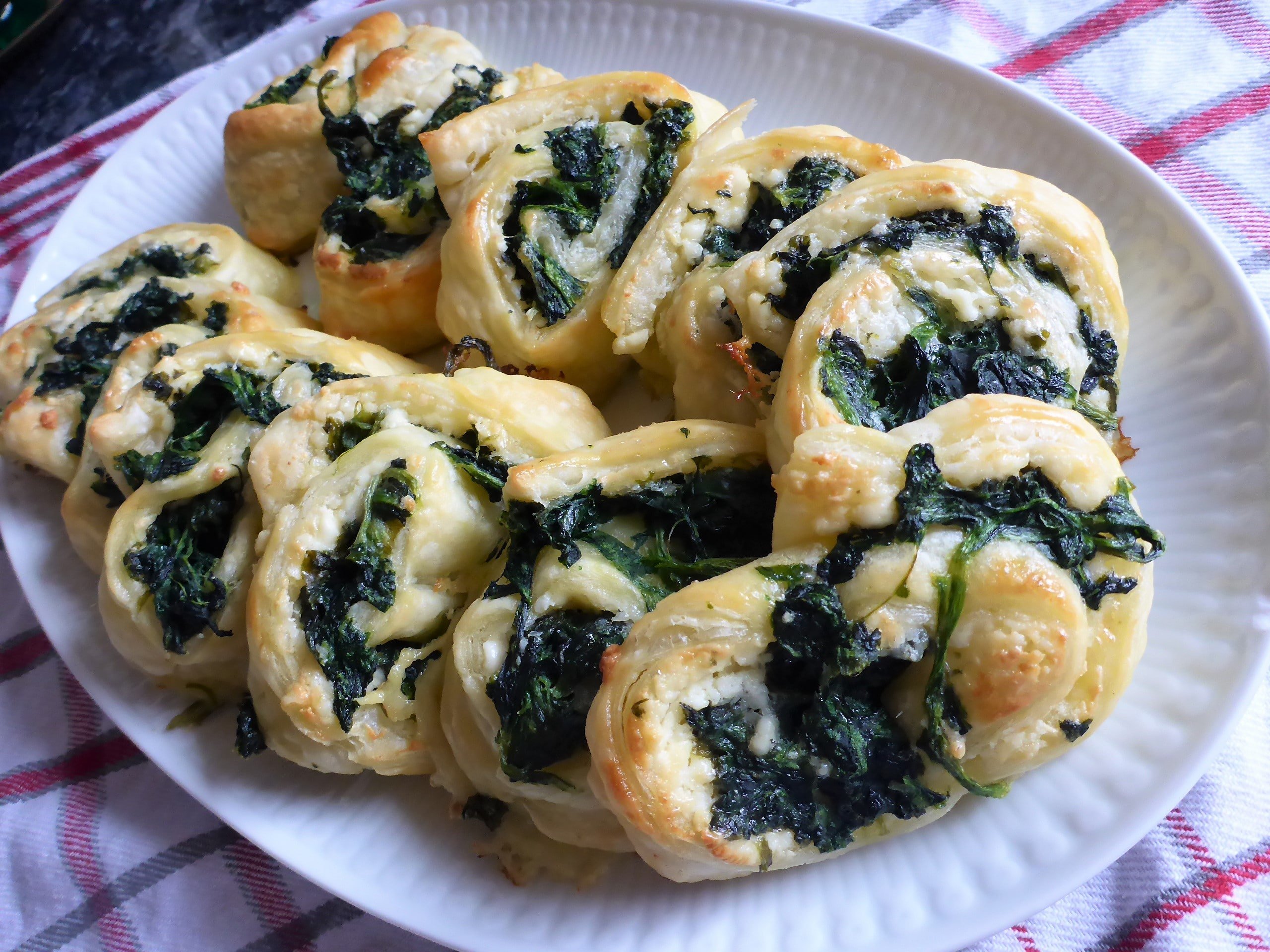 Auf dem Bild sind frisch gebackene Spinat und Feta Blätterteigschnecken  vegetarisch  zu sehen, die auf einer Tellerplatte sind.