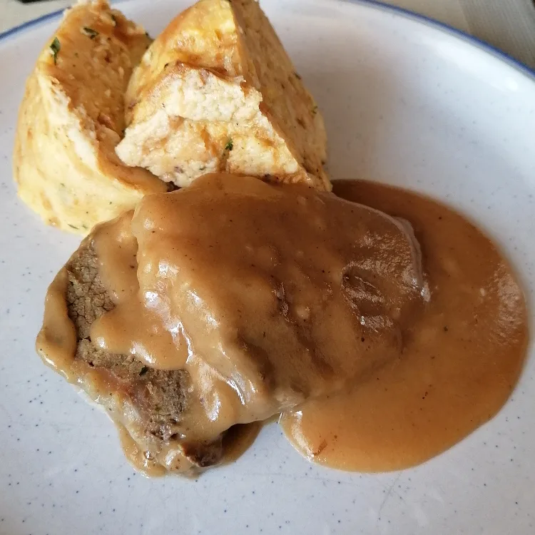 A beautifully plated German braised beef dish with sauerbraten sauce, served alongside Serviettkloß, also known as bread dumplings.