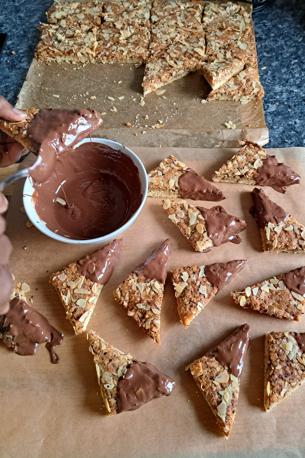 Dipping German nut cookies cut into triangles in melted chocolate. 