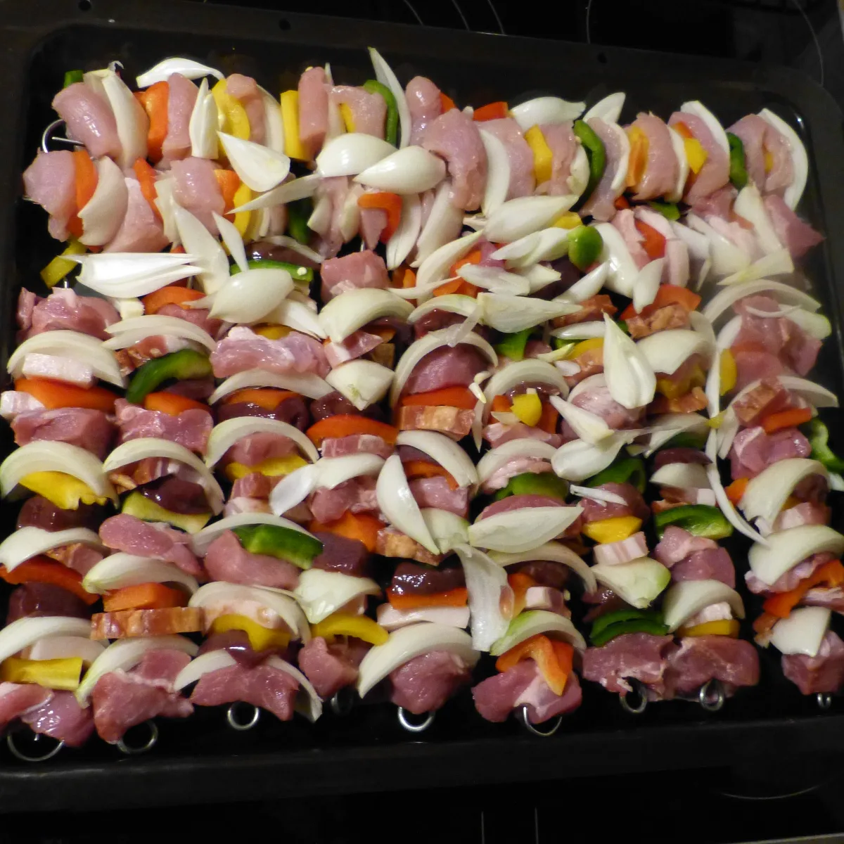 Jede Menge Schweinespieße auf einem Backblech vor dem Kochen. 