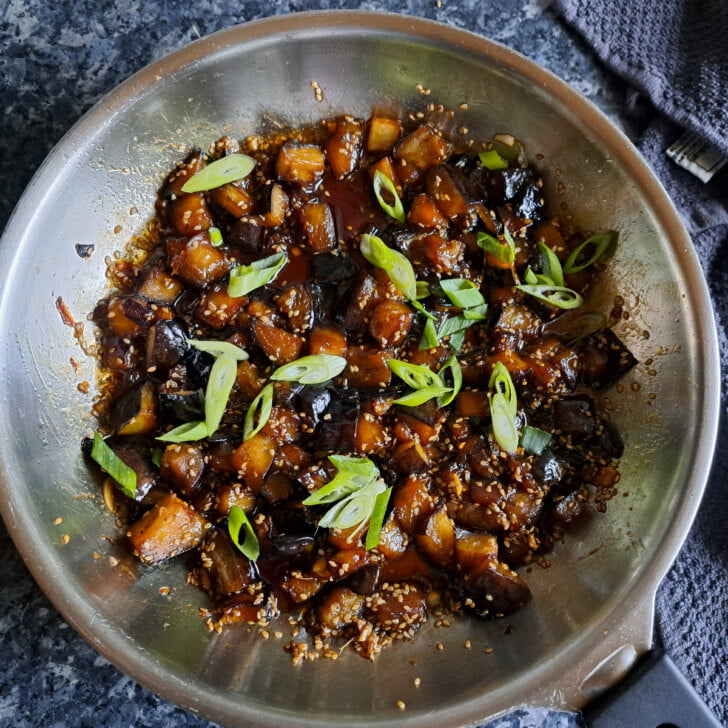 Asiatische gebratene Aubergine in einer Pfanne garniert mit Frühlingszwiebeln.