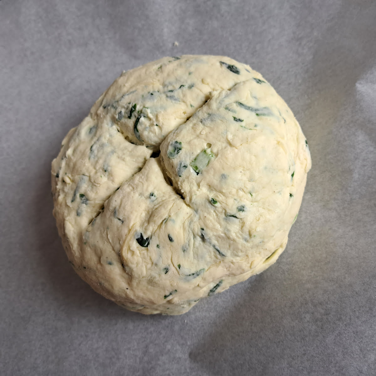 Wild garlic bread dough with a cross on the top of the bread loaf, before baking.