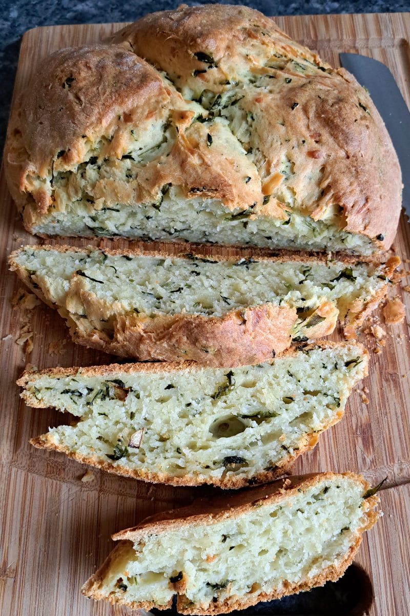 Freshly baked cheesy wild garlic bread on a cutting board, sliced and ready to serve. 