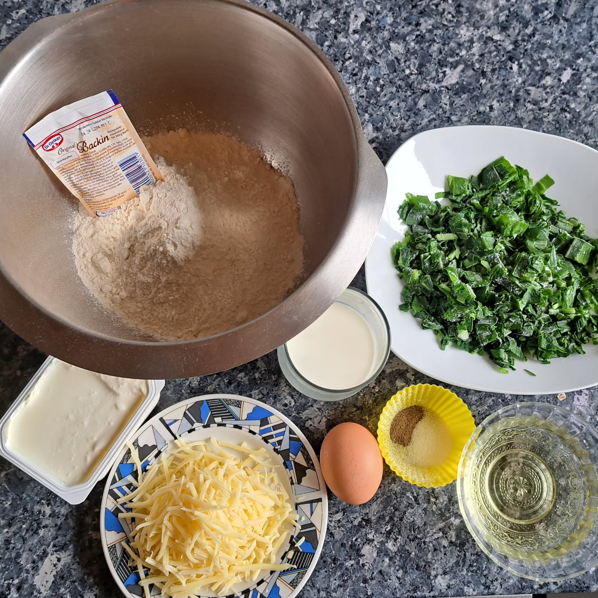 Ingredients for making wild garlic bread: Fkour, baking powder, quark, oil, egg, wild garlic, cheese and salt, arranged on the kitchen counter. 