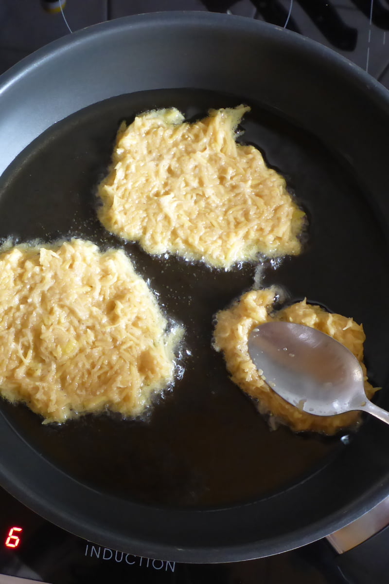 Kartoffelpuffer Masse mit der Rückseite des Löffels plattdrücken.