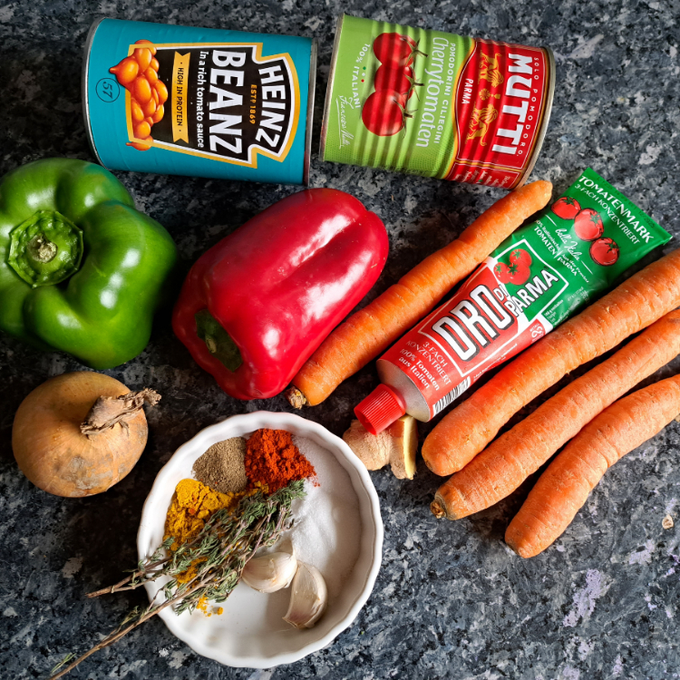 A photo of the ingredients used to make chakalaka, a popular South African vegetable relish, on a kitchen counter. The ingredients include bell peppers, grated carrots, baked beans, garlic, fresh ginger, onion, tomato paste, thyme, paprika, curry powder, ground pepper, salt, sugar, canned tomatoes, and oil. These ingredients are often combined to create a flavorful and versatile dish that can be enjoyed as a side dish or a main meal with a variety of foods.