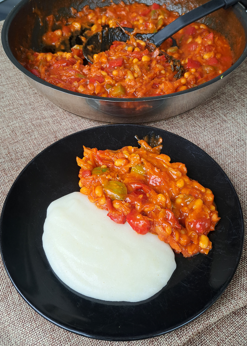 A photo of a pan with freshly cooked chakalaka and a plate of pap, a traditional South African porridge made from maize meal, on a table at a balcony.