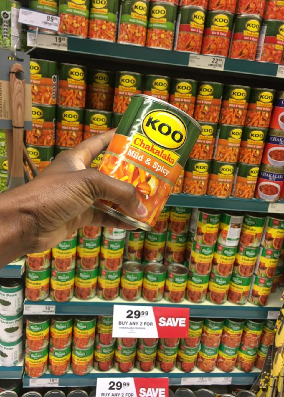 A photo of different cans of chakalaka relish with varying levels of spiciness, ranging from mild to extra hot, on a shelf in a Namibian supermarket.