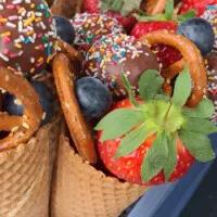 Kunterbunte-Eistüte-ist-gefüllt-mit-frischem-Obst-und Kuchen am Stiel (Cake pops).