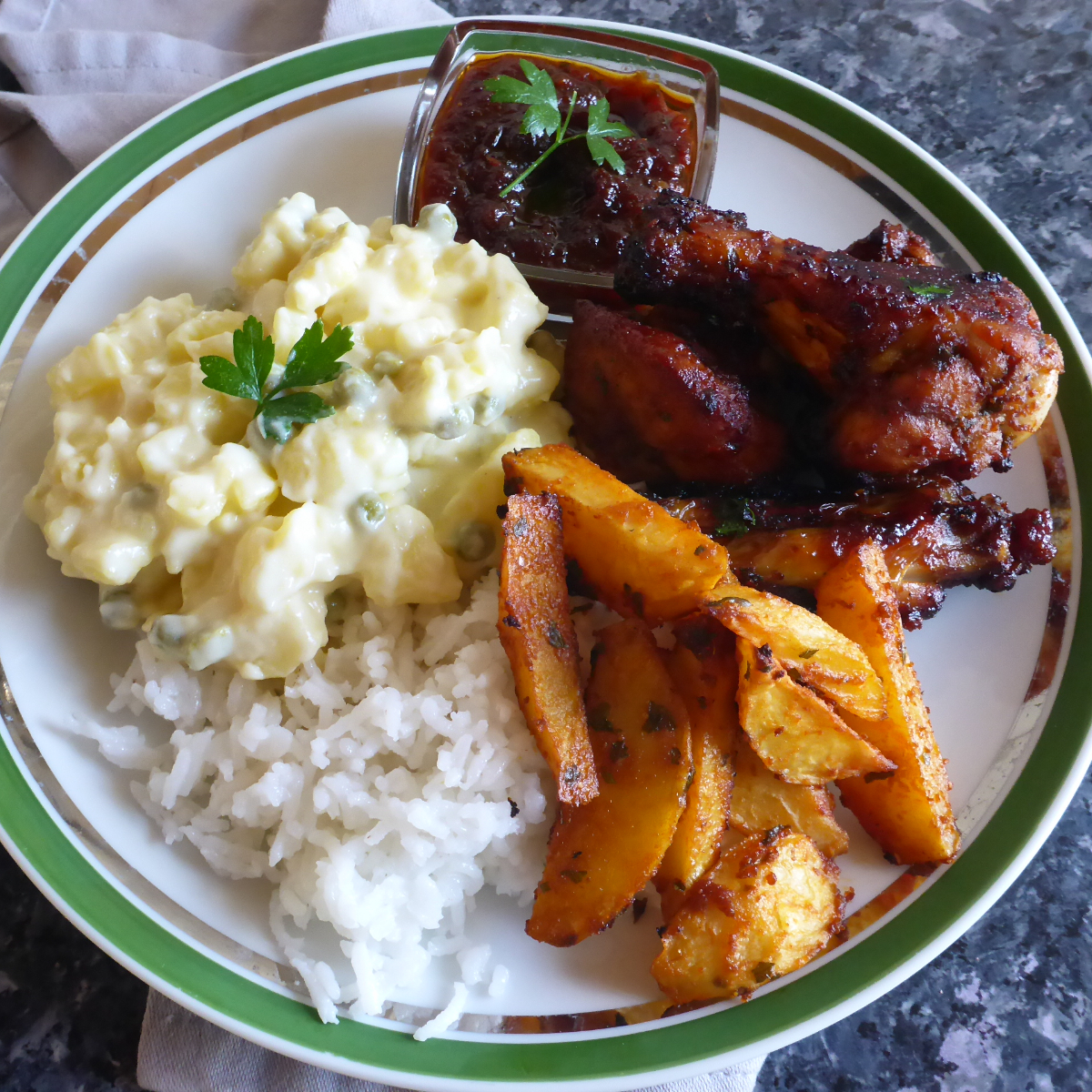 A well-balanced plate featuring a succulent roasted chicken, crispy roasted potatoes, fluffy white rice, creamy Namibian potato salad, and a small bowl of flavorful dipping sauce.