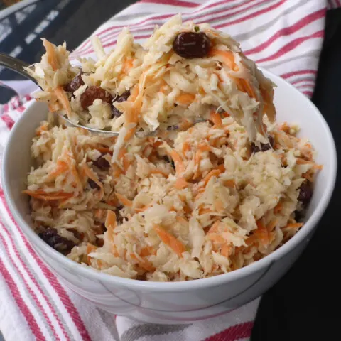 A vibrant bowl of freshly made Namibian-style coleslaw salad, featuring crisp cabbage, grated carrots, plump raisins, and a creamy dressing, creating a colorful and appetizing dish.