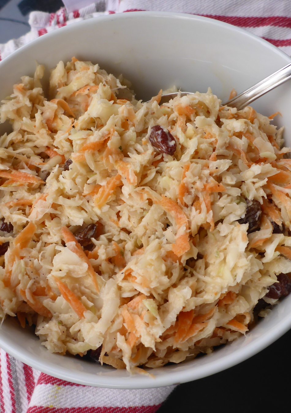 A vibrant bowl of freshly made Namibian-style coleslaw salad, featuring crisp cabbage, grated carrots, plump raisins, and a creamy dressing, creating a colorful and appetizing dish.