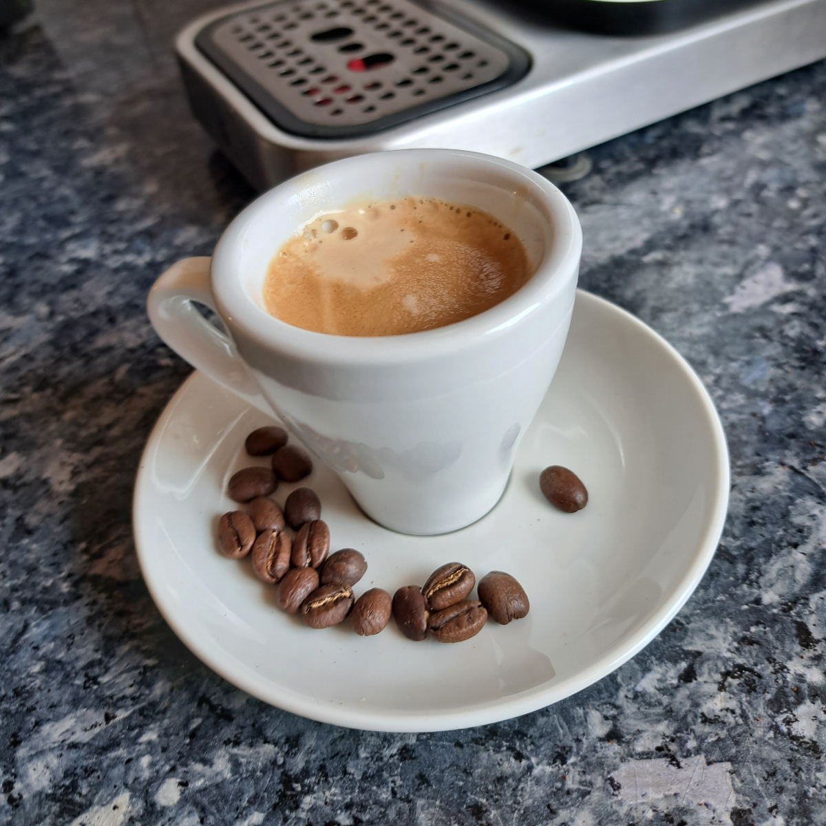 Frisch zubereiteten Espresso in einer Espressotasse, umgeben von Kaffeebohnen auf einem Espresso-Unterteller.