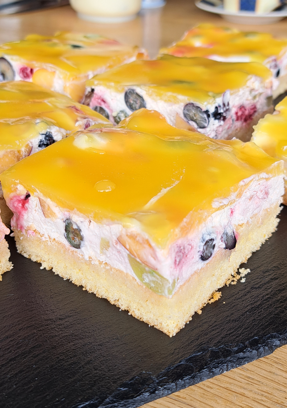 Slice of delicious German fresh cream fruit cake topped with an assortment of vibrant fruits and an orange juice glaze, served on a plate.