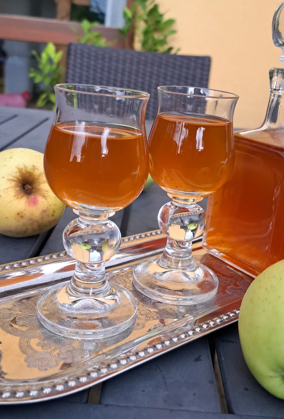 Two glasses filled with insanely delicious homemade apple liqueur, garnished with apple slices, and a full bottle of the liqueur in the background. 