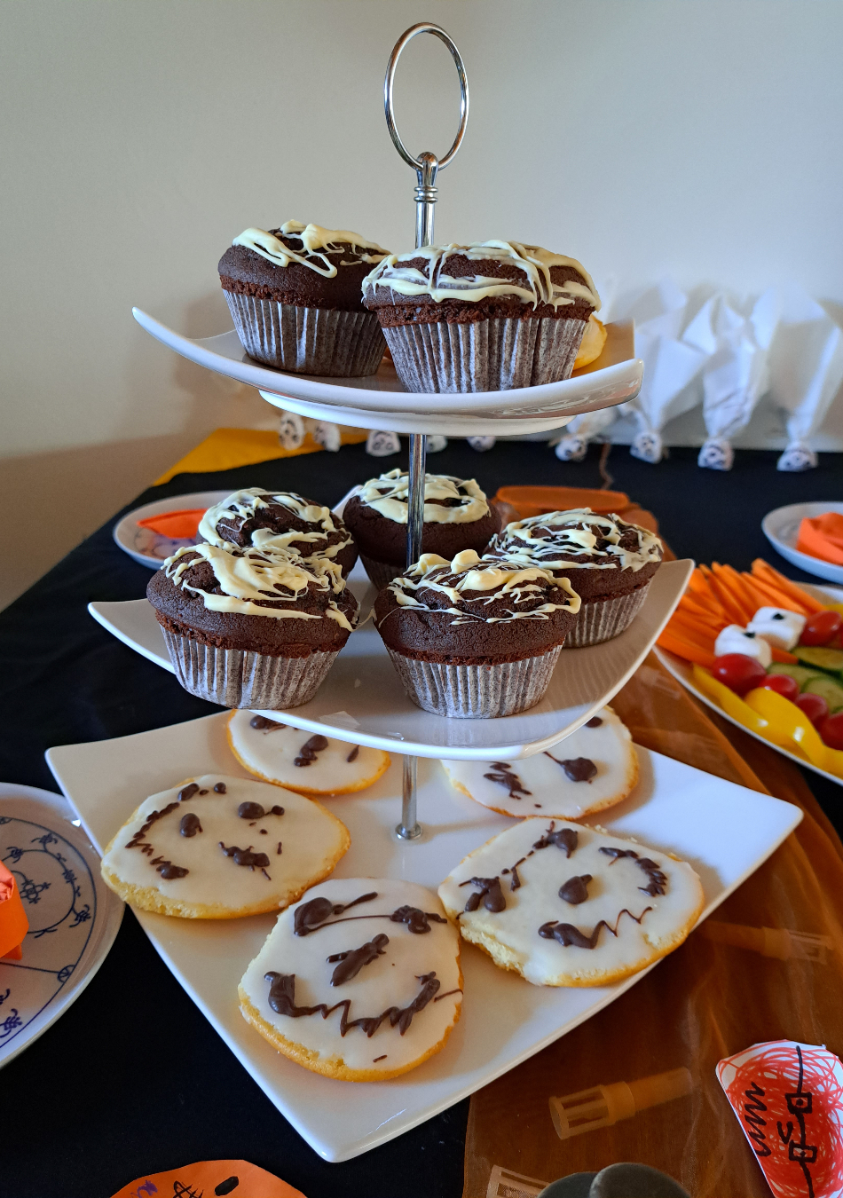 Selbstgemachte Mini-Amerikaner, überzogen mit Zuckerguss und von Hand mit geschmolzener Zartbitterschokolade verziert. Und selbstgemachte Schokomuffins mit einem Spinnennetz aus geschmolzener weißer Schokolade auf der Oberseite.