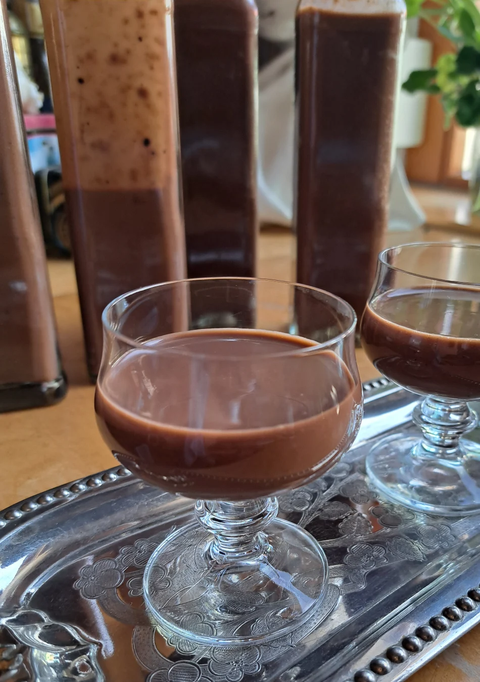 Glass filled with velvety homemade chocolate egg liqueur, surrounded by tempting bottles of the exquisite liqueur in the background, showcasing a delightful array of indulgent treats.