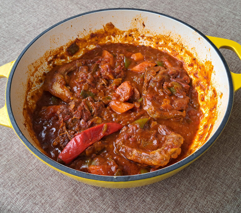 Image of a yellow cast iron pot of lamb potjie containing fall-apart tender lamb immersed in an incredibly rich and deep-flavored sauce.