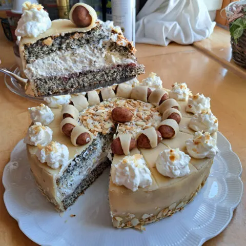 Ein Bild zeigt eine wunderschöne Mohn-Marzipan-Torte, auf der ein Stück der Torten mit einem Tortenheber angehoben wird.