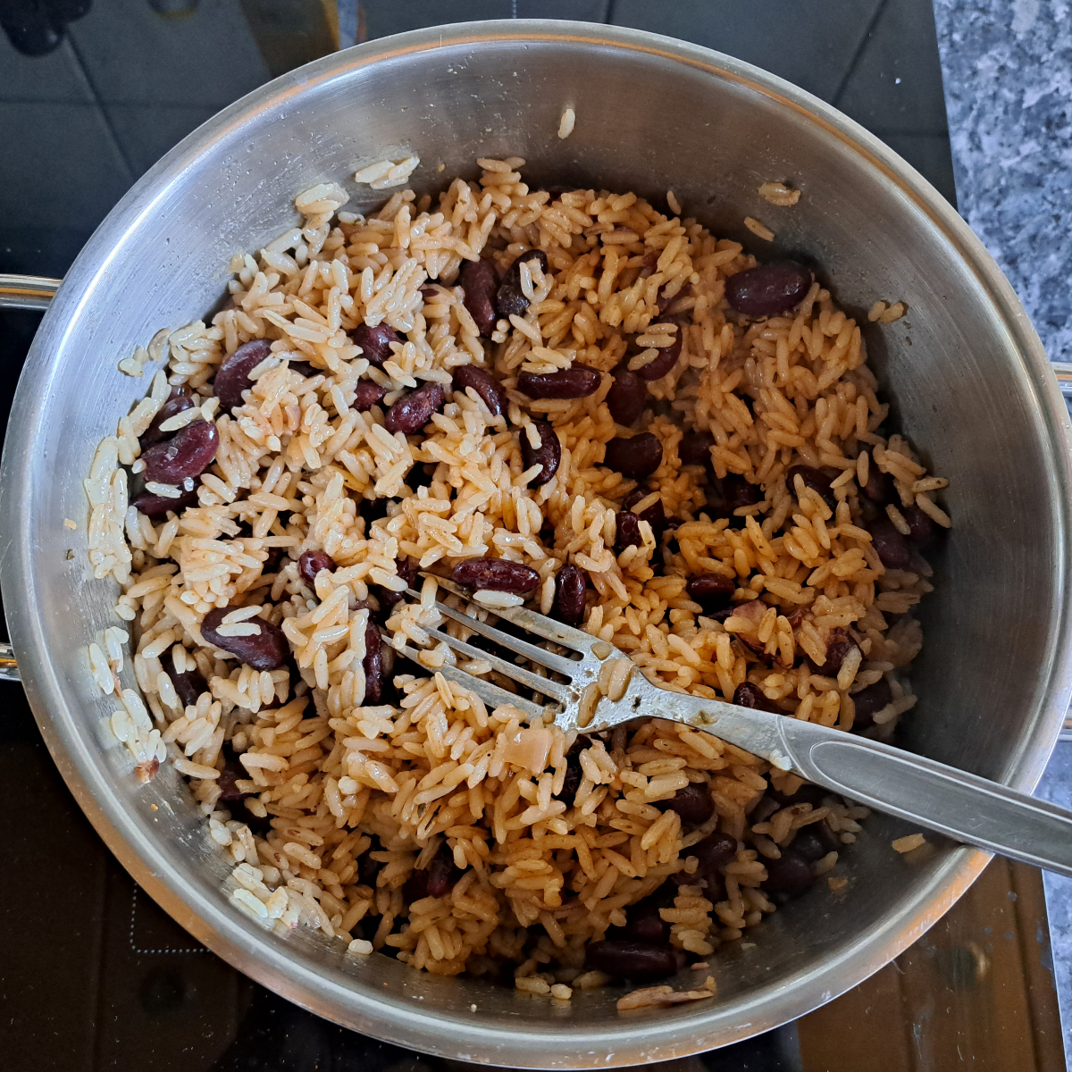 Ein Bild zeigt frisch gekochten jamaikanischen Reis mit Kidneybohnen in einem Topf, aufgelockert mit einer Gabel.