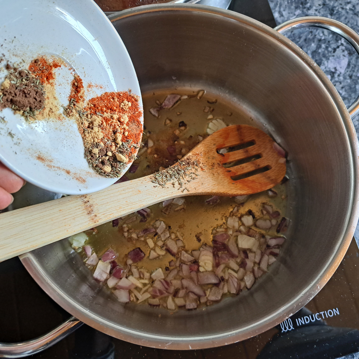 Ein Bild zeigt einen größeren Topf mit gebratenen Zwiebeln und Knoblauch, dazu werden Gewürze in weißen Schälchen hinzugefügt. Dies ist der Grundschritt für die Zubereitung von jamaikanischem Reis mit Kidneybohnen.