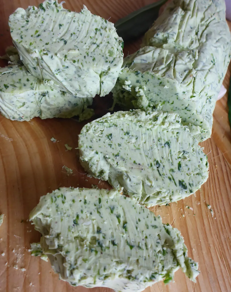 Slices of homemade herbed butter with wild garlic neatly arranged on a plate, showcasing its vibrant green color and creamy texture