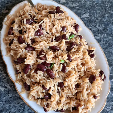 Ein Bild zeigt leckere jamaikanischen Reis mit Kidneybohnen auf einer weißen Platte, bereit um serviert zu werden. Auf der Platte ist eine Gabel mit etwas Reis.