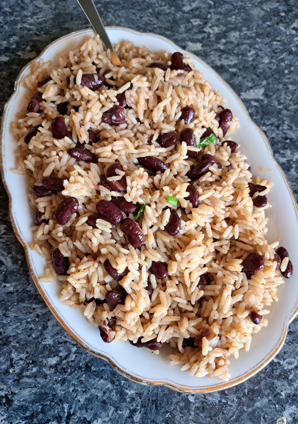 Ein Bild zeigt frisch gekochten jamaikanischen Reis mit Kidneybohnen auf einer weißen Platte auf einer Küchenbank.