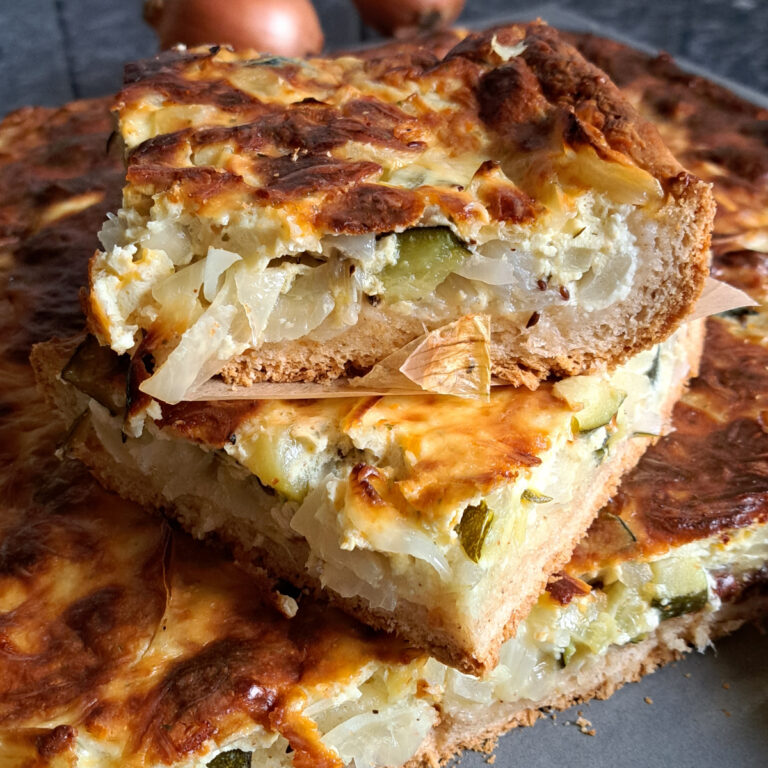 A freshly baked German onion cake (Zwiebelkuchen), golden brown on top, cut into slices and arranged on a tray, showcasing the crisp crust and savory filling.