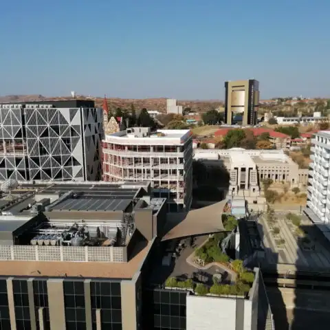 A breathtaking view of Windhoek from the top floor of Avani Hotel, showcasing the city's high-rise buildings, the historic Christuskirche, and the striking Independence Memorial Museum, built by North Korea. The cityscape blends modern and historical architecture against the scenic backdrop of the Namibian capital.