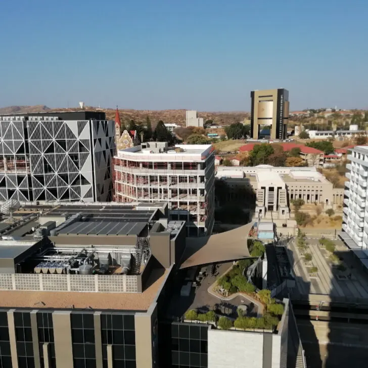 A breathtaking view of Windhoek from the top floor of Avani Hotel, showcasing the city's high-rise buildings, the historic Christuskirche, and the striking Independence Memorial Museum, built by North Korea. The cityscape blends modern and historical architecture against the scenic backdrop of the Namibian capital.