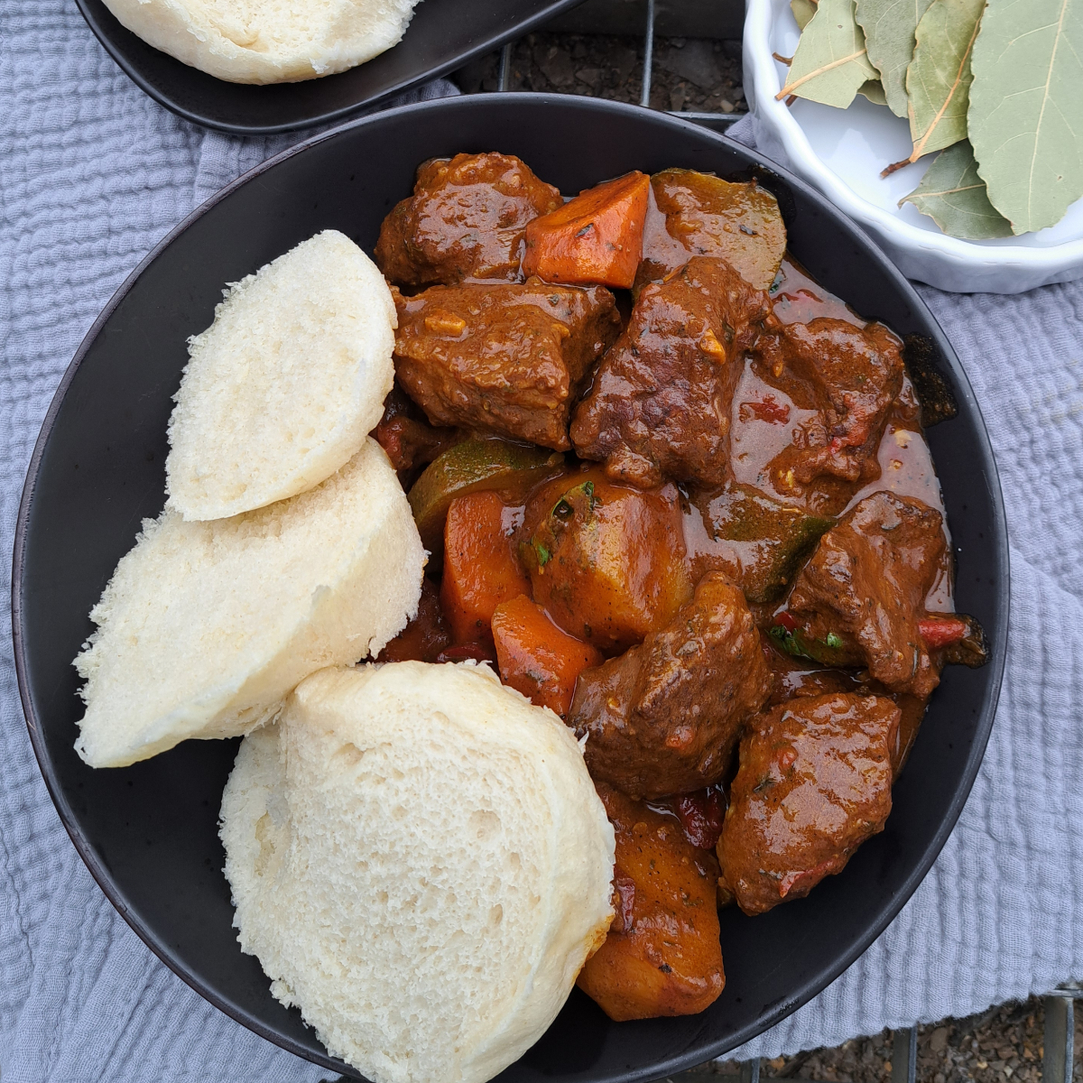 A plate of African steamed bread served alongside rich, flavorful beef stew, garnished with herbs.