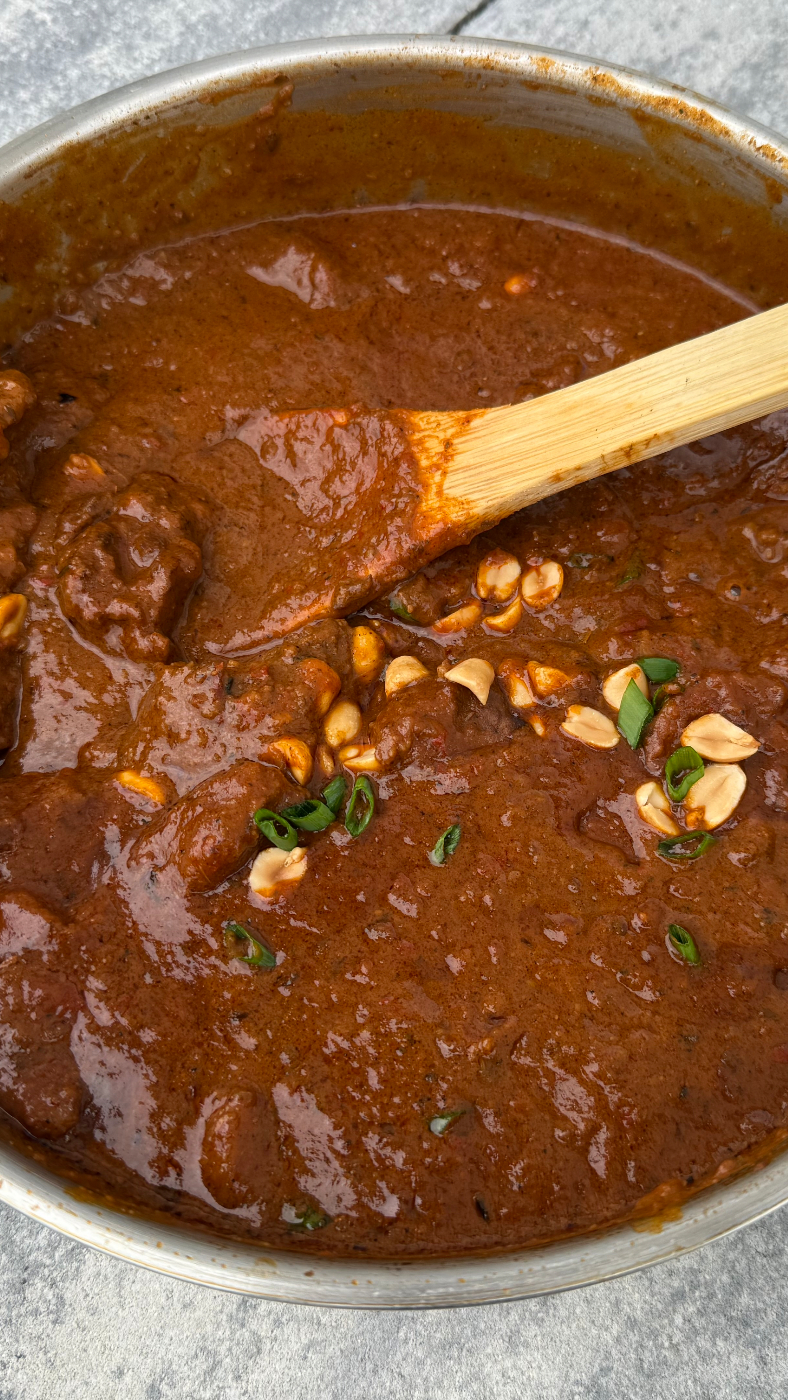 Servierbereiter afrikanischer Erdnuss-Eintopf im Topf mit gerösteten Erdnüssen und Frühlingszwiebeln garniert