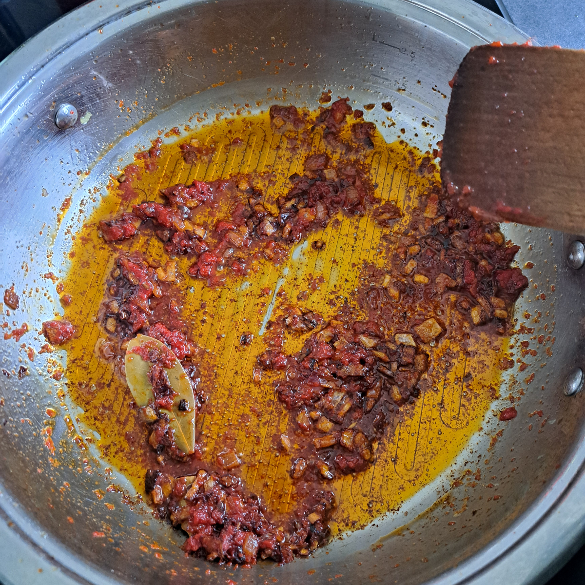 Zwiebeln, Tomatenmark, und Lorbeerblätter werden im Topf angebraten für die Basissoße eines Jollof Reis Rezeptes