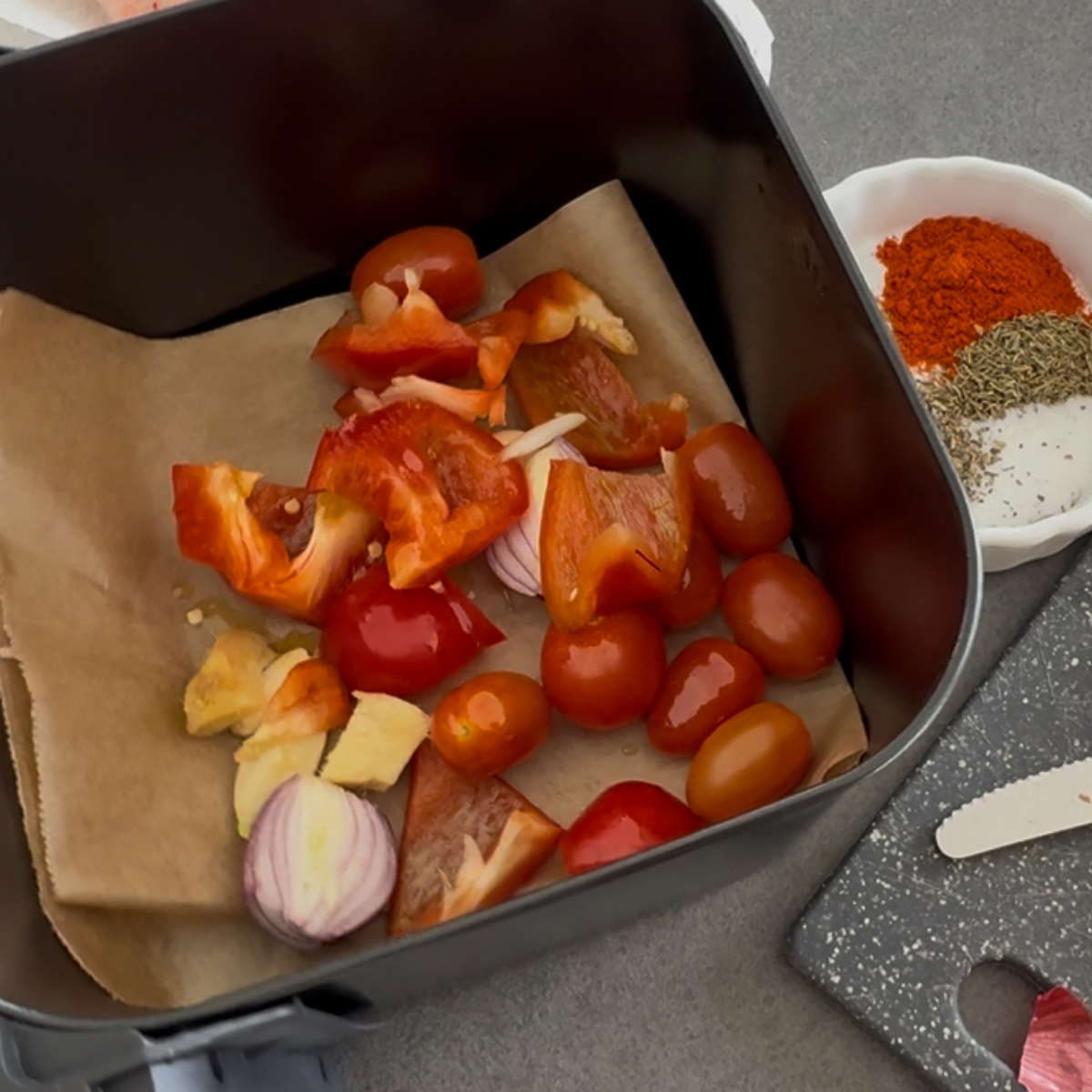 Geschnittene Paprika, Tomaten, Zwiebeln, Ingwer und Knoblauch mit Olivenöl in der Heißluftfritteuse vor dem Rösten für afrikanisches Ofenhähnchen.