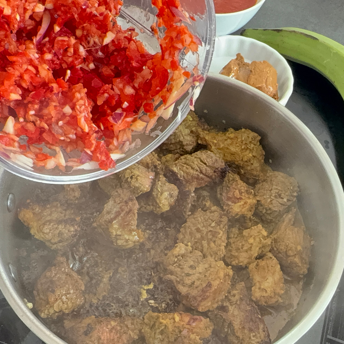 Zwiebeln, Knoblauch, Ingwer und Paprika werden zu gebräuntem Rindfleisch im Topf gegeben