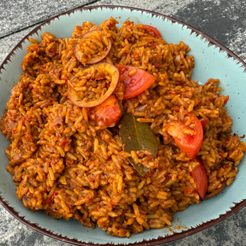 Gekochter Jollof Reis in einer Schüssel mit sichtbaren Tomaten und Zwiebeln als Garnitur